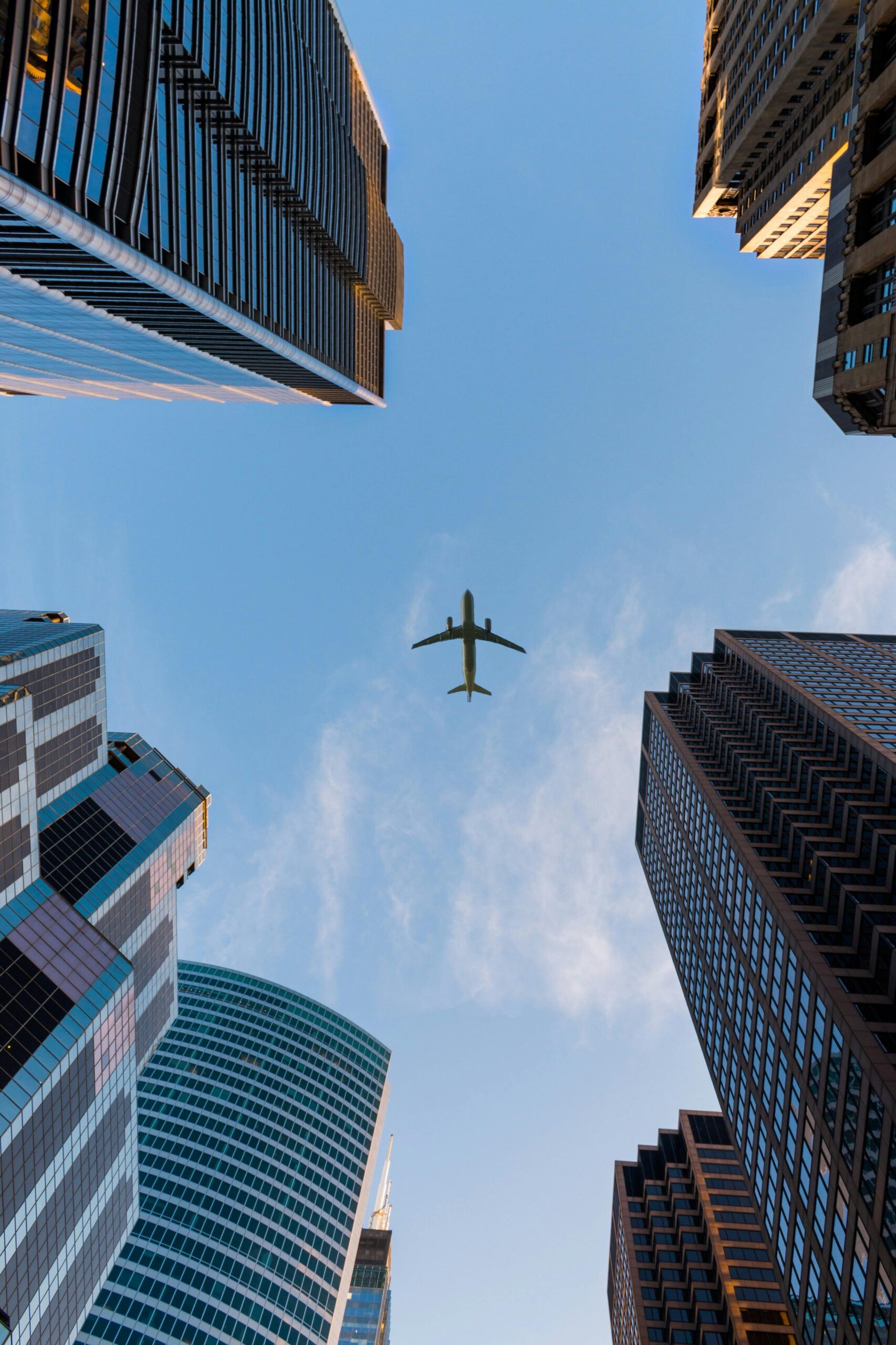 Airplane flies over Chicago's modern skyscrapers against a clear sky, highlighting urban architecture.